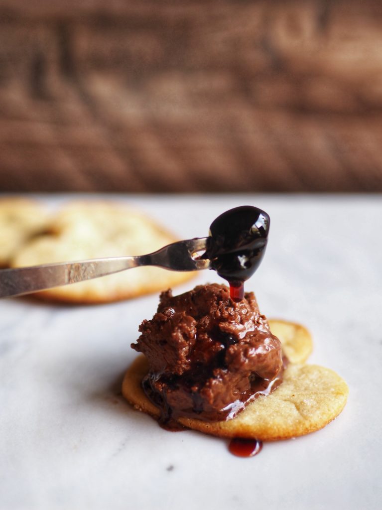 Luxardo dark cherries dripping syrup onto scoop of mousse on heart shaped pie crust cutout. 