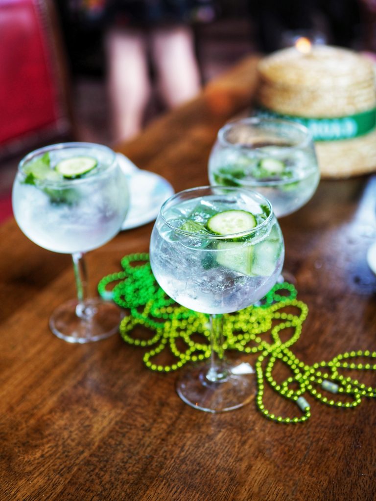 Dingle Irish Gin, Fever Tree Elderflower Tonic, Fresh Lime, Cucumber, Mint in a large wine goblet with cucumber and mint on a table with Irish beads and a Raglan Road Irish Hat