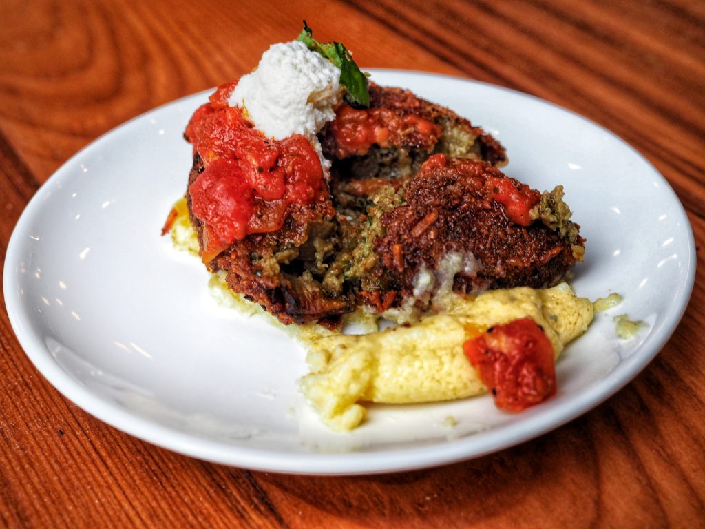 roasted eggplant (vegetarian) "meatball", and the traditional combination of pork and beef. Both options are served with tomato sauce over polenta and topped with ricotta and fresh basil